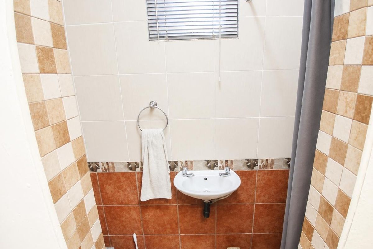 A compact bathroom featuring a wall-mounted basin, tiled walls with decorative accents, and a window with a venetian blind.