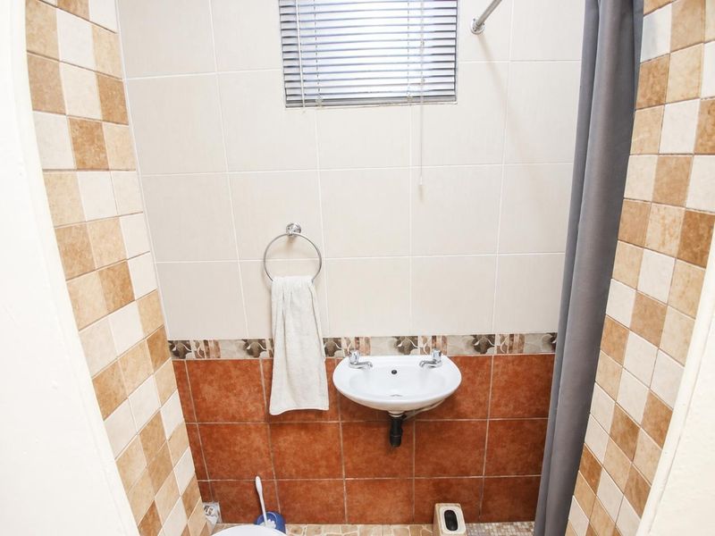 A compact bathroom featuring a wall-mounted basin, tiled walls with decorative accents, and a window with a venetian blind.