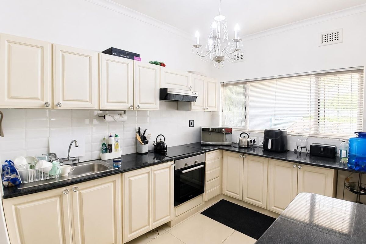 A functional kitchen featuring cream-colored cabinetry, dark granite countertops, a built-in oven, and a tiled backsplash with ample natural light.