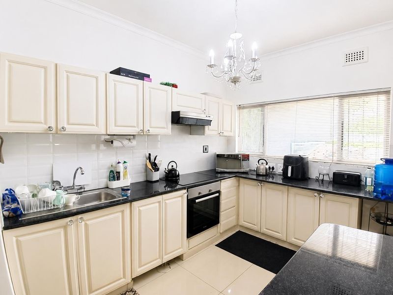 A functional kitchen featuring cream-colored cabinetry, dark granite countertops, a built-in oven, and a tiled backsplash with ample natural light.