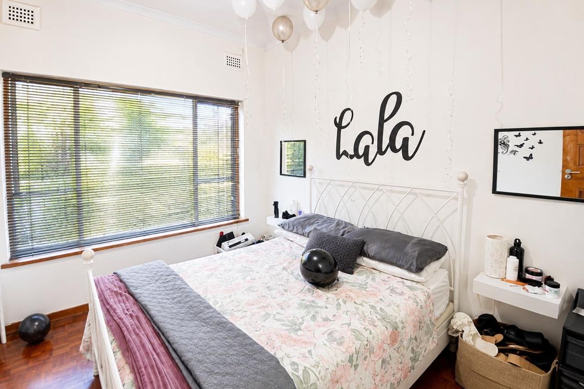 A well-maintained bedroom featuring polished timber flooring, large window with venetian blinds, and classic cornice detailing.