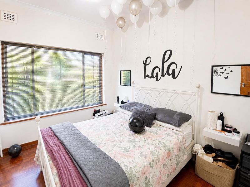 A well-maintained bedroom featuring polished timber flooring, large window with venetian blinds, and classic cornice detailing.