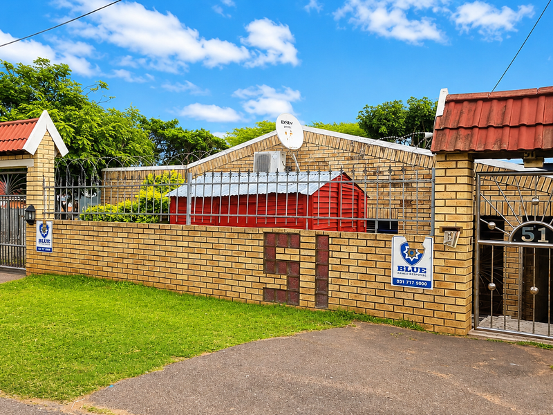 Front exterior view of a face brick house featuring a secure boundary wall, metal gates, and tiled entrance pillars.