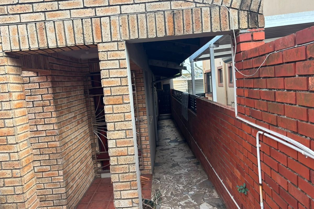 A narrow exterior side passage featuring face brick walls, a stone paved walkway, and a security gate entrance.