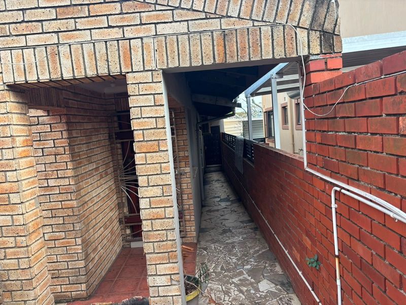 A narrow exterior side passage featuring face brick walls, a stone paved walkway, and a security gate entrance.
