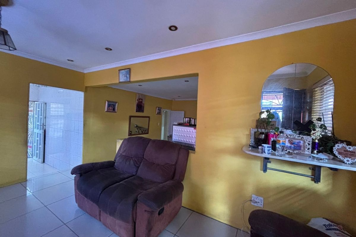 A living room area featuring tiled flooring, recessed downlighting, and a wall-mounted shelf, with an open-plan layout connecting to adjacent spaces.