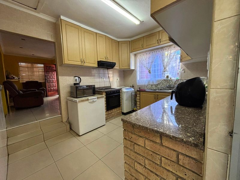 A functional kitchen featuring built-in cabinetry, granite countertops, a brick breakfast bar, and tiled flooring, offering a practical layout with direct access to the living area.