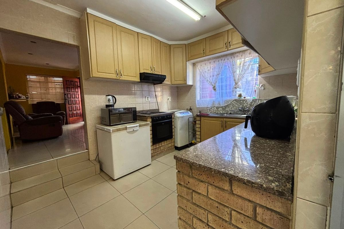 A functional kitchen featuring built-in cabinetry, granite countertops, a brick breakfast bar, and tiled flooring, offering a practical layout with direct access to the living area.