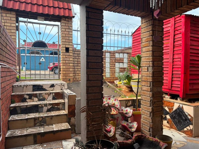 A covered outdoor patio area featuring brick pillars, tiled stairs with decorative finishes, and a secure gated entrance with perimeter razor wire fencing.