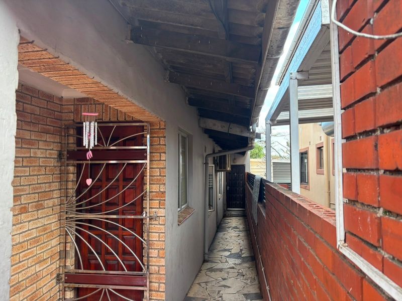 A narrow exterior side passage featuring brick walls, a security gate, and paved flooring with exposed timber roof rafters.