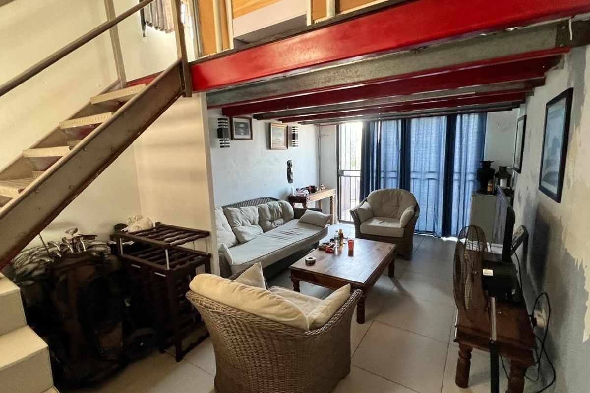 Open-plan living area featuring exposed red steel beams, a metal staircase, and tiled flooring with direct access to an outdoor space.