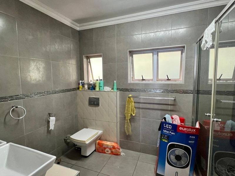 A modern bathroom featuring full-height wall tiling, a wall-mounted toilet, and a glass-enclosed shower with natural light from casement windows.