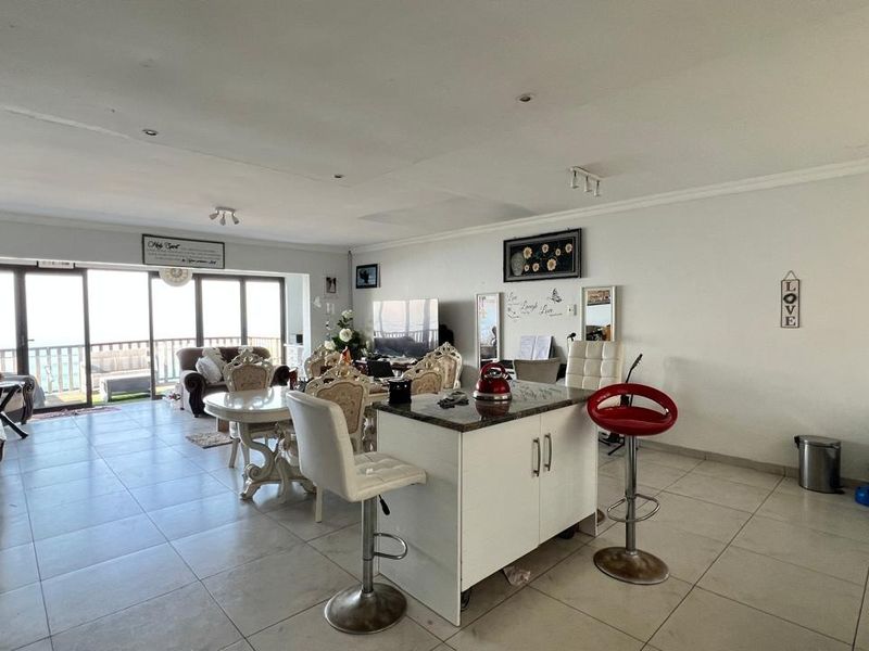 Spacious open-plan living and kitchen area featuring tiled floors, a central kitchen island with granite countertop, and large sliding doors leading to a balcony.