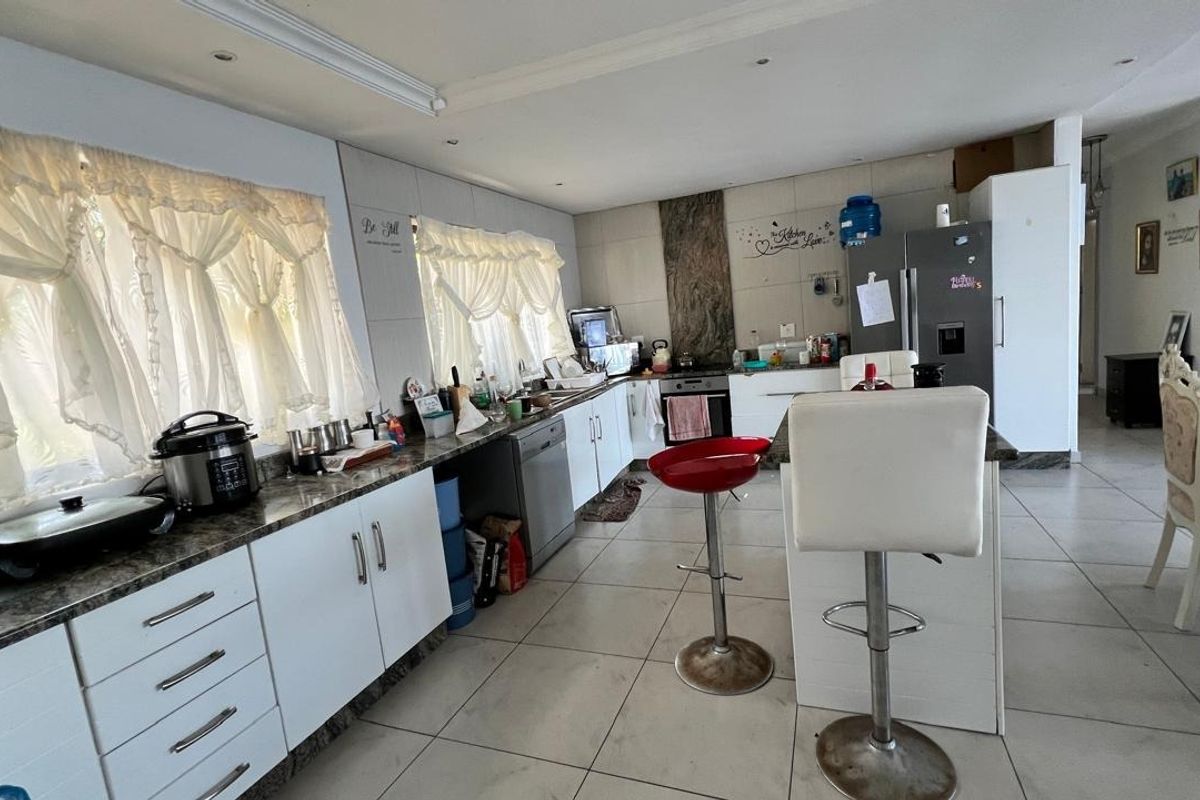 Spacious kitchen featuring white cabinetry, granite countertops, a central island, and tiled flooring, offering a functional layout for cooking and casual dining.