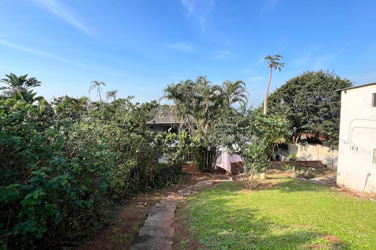 Rear garden area featuring a lawn, concrete pathway, and established trees, adjacent to the side elevation of the property.