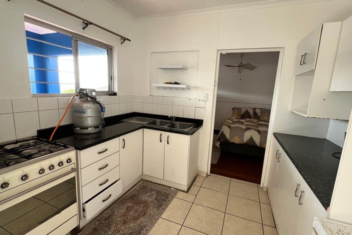 Functional kitchen featuring white cabinetry, dark laminate countertops, a gas stove, and tiled flooring with direct access to an adjacent bedroom.