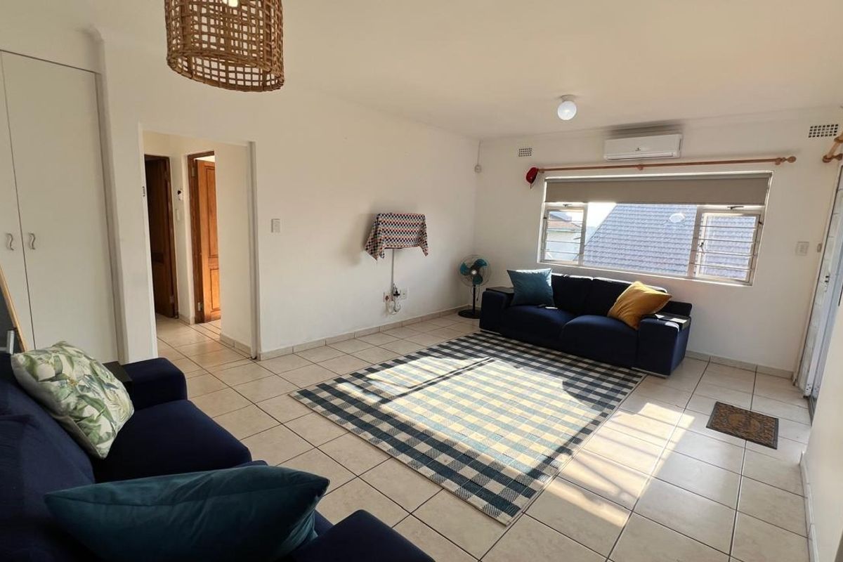 A bright living room featuring tiled flooring, a split-system air conditioner, and built-in storage cupboards.