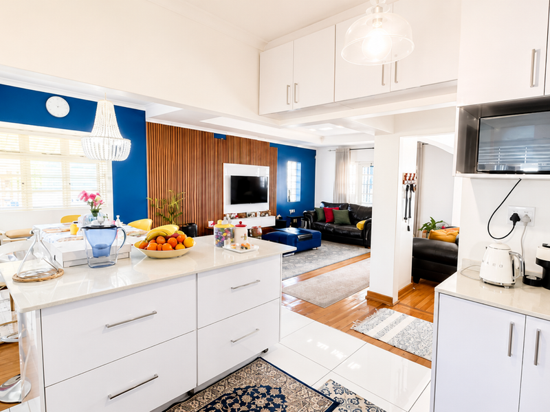 A bright open-plan living and kitchen area featuring a central island, modern cabinetry, timber feature wall, and a seamless blend of hardwood and tiled flooring.
