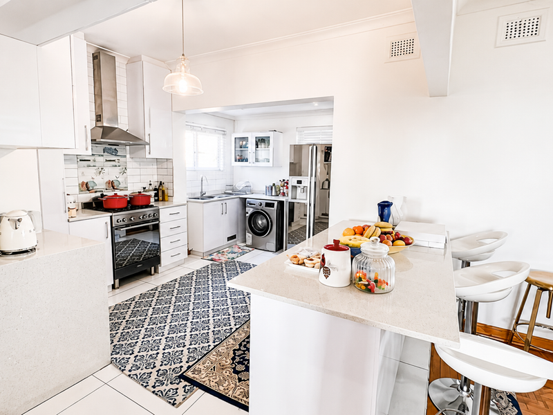 Bright open-plan kitchen featuring a central island with stone countertops, modern cabinetry, stainless steel appliances, and a seamless transition to the laundry area.