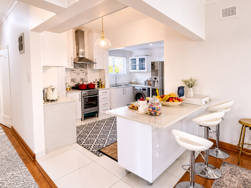 Bright open-plan kitchen featuring a central island, modern cabinetry, stainless steel appliances, and tiled flooring, seamlessly connecting to the living and dining areas.