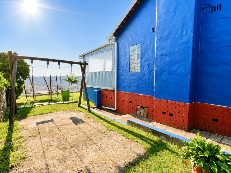 Rear exterior view of the property featuring a blue painted facade, brick foundation, and a garden area with a swing set.