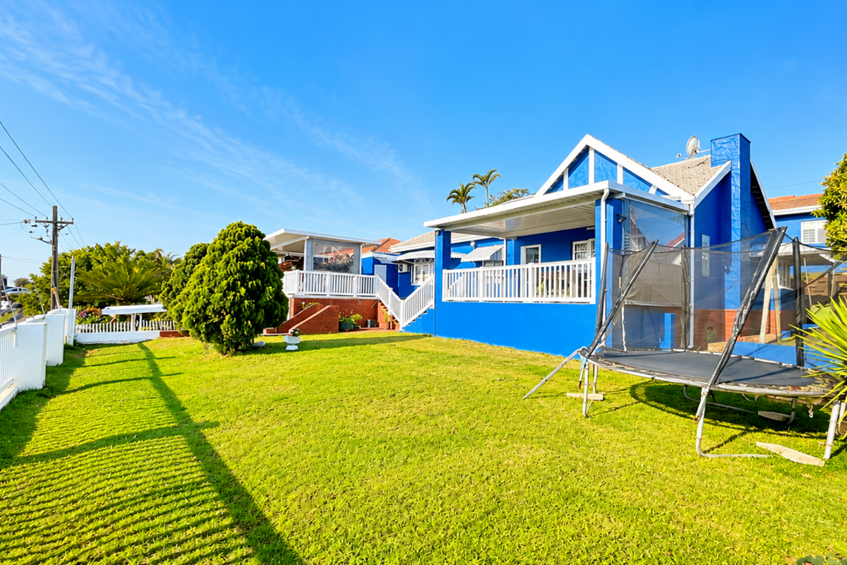 Rear view of a blue-painted house featuring a raised patio with white balustrades, a tiled roof, and a well-maintained lawn.