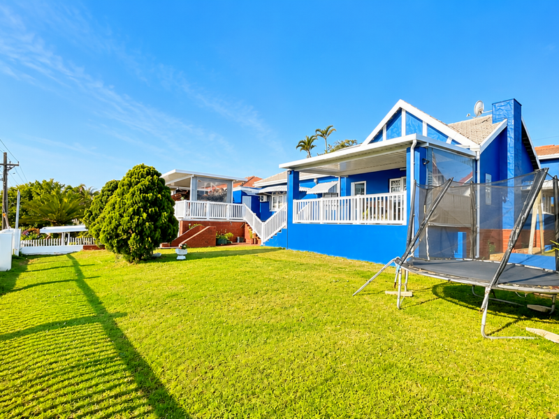 Rear view of a blue-painted house featuring a raised patio with white balustrades, a tiled roof, and a well-maintained lawn.