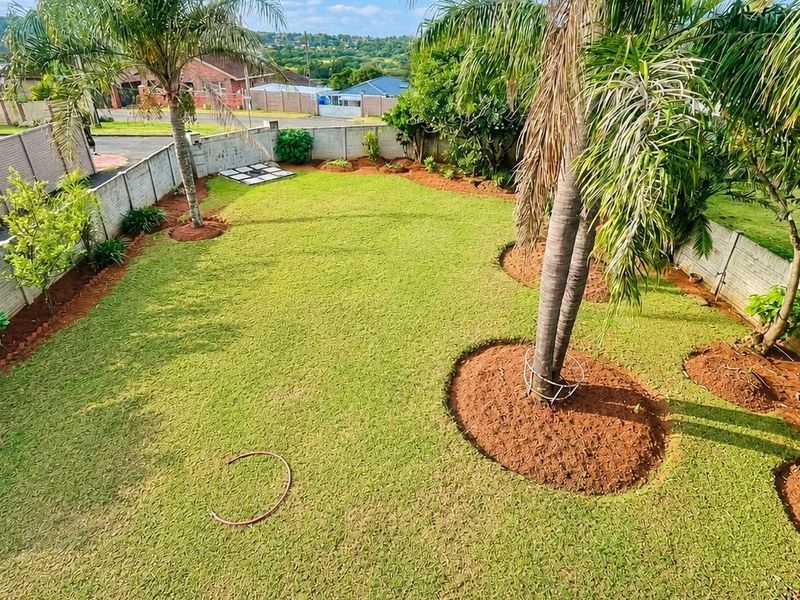 A well-maintained, spacious private garden featuring a manicured lawn, mature palm trees, and secure precast concrete boundary walls.