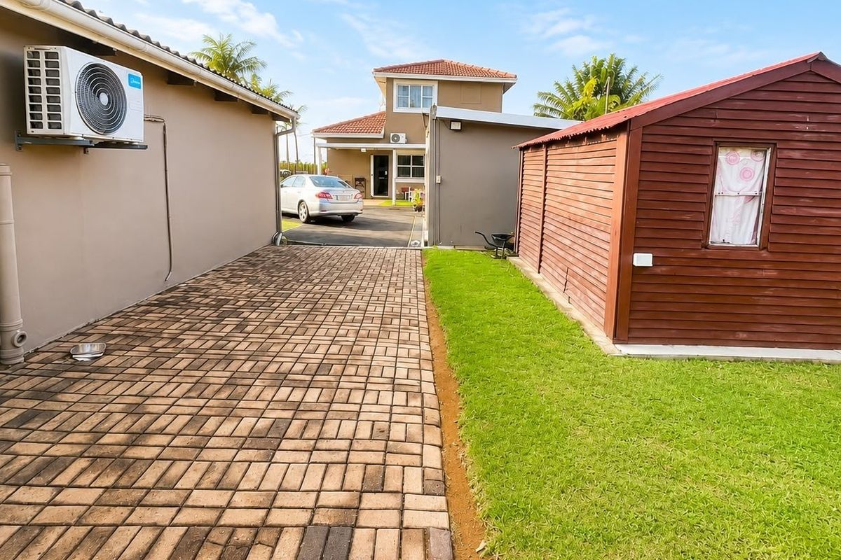 A view of the rear exterior featuring a paved driveway, a well-maintained lawn, and a detached wooden storage shed.