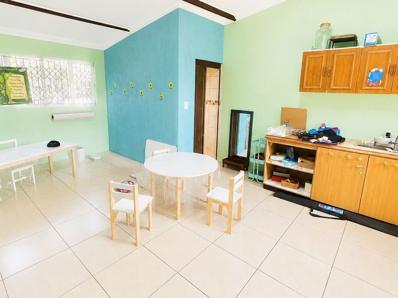 A functional kitchen area featuring built-in wooden cabinetry, a stainless steel sink, and tiled flooring, with large windows providing natural light.