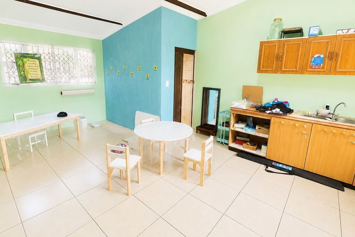 A functional kitchen area featuring built-in wooden cabinetry, a stainless steel sink, and tiled flooring, with large windows providing natural light.