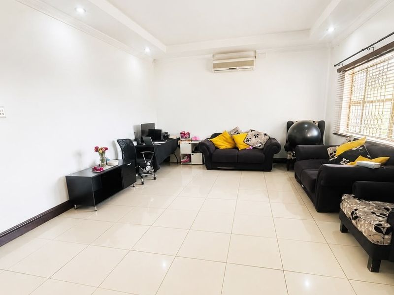 A spacious living room featuring neutral tiled flooring, recessed ceiling lighting, and a wall-mounted air conditioning unit, providing a comfortable and functional living space.