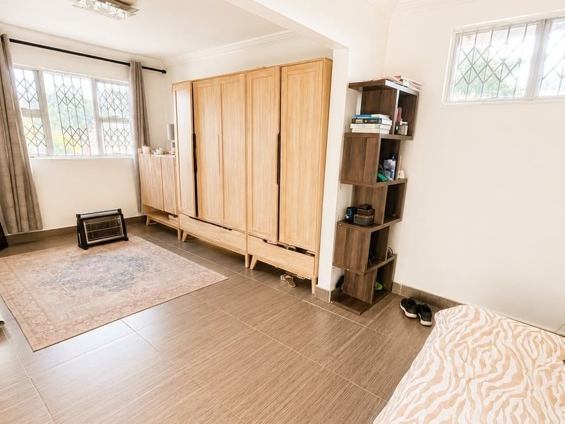 A spacious bedroom featuring neutral tiled flooring, built-in wooden wardrobes, and windows fitted with security bars for added peace of mind.