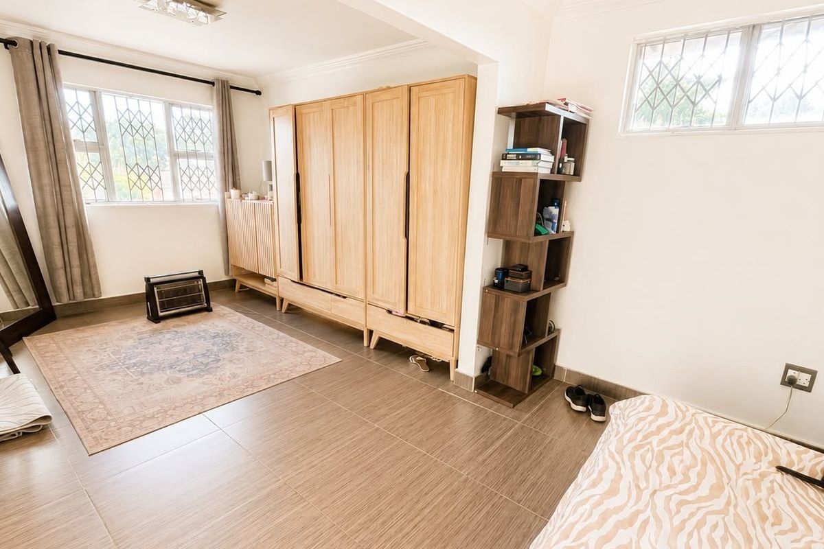 A spacious bedroom featuring neutral tiled flooring, built-in wooden wardrobes, and windows fitted with security bars for added peace of mind.