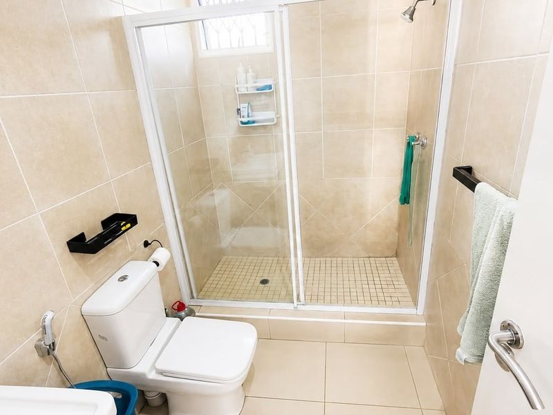 A functional bathroom featuring a glass-enclosed shower, tiled walls and flooring, and modern sanitary fixtures.