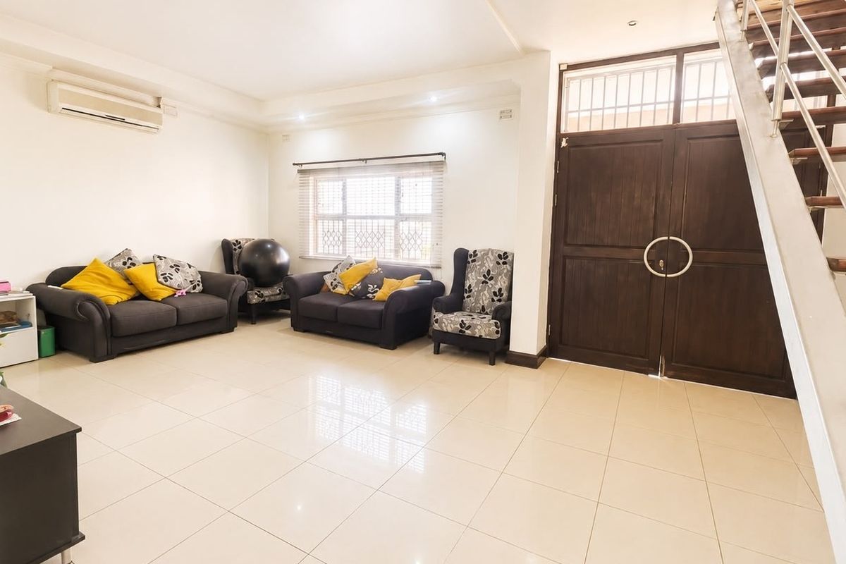 Spacious living room featuring tiled flooring, a split-system air conditioner, and a prominent staircase with a metal railing leading to the upper level.