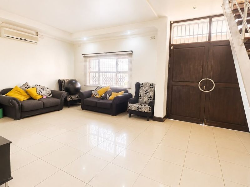 Spacious living room featuring tiled flooring, a split-system air conditioner, and a prominent staircase with a metal railing leading to the upper level.