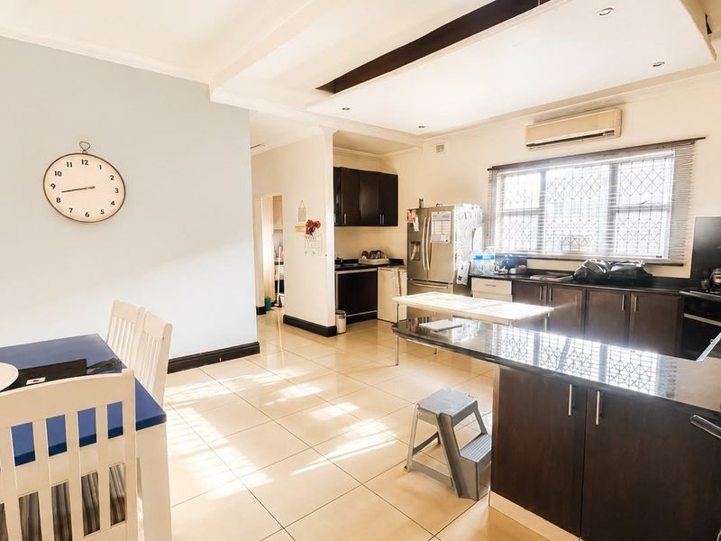 Spacious open-plan kitchen and dining area featuring dark wood cabinetry, granite countertops, tiled flooring, and integrated air conditioning.