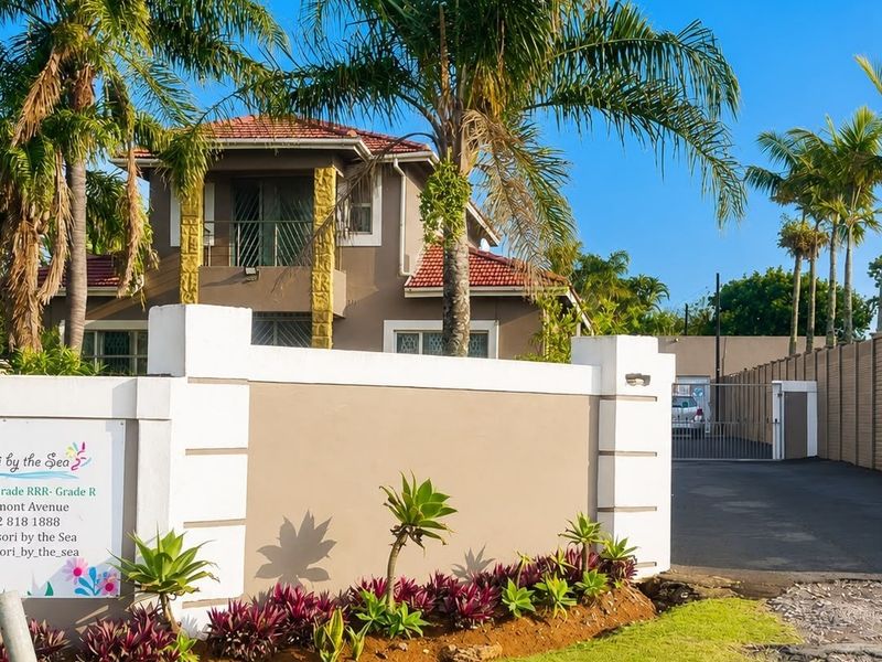 Front exterior view of the property featuring a boundary wall, paved driveway, and a two-story building with a tiled roof and balcony.