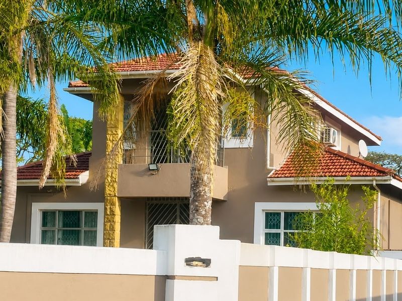 A two-story residential house featuring a terracotta tiled roof, a front balcony, and a secure perimeter wall with gated access.