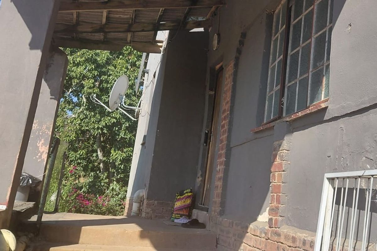 A covered patio area featuring brick masonry and steel window frames, currently showing signs of significant wear and requiring maintenance to the exterior finishes.