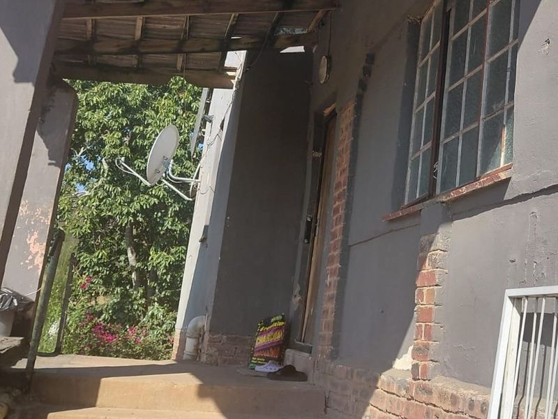 A covered patio area featuring brick masonry and steel window frames, currently showing signs of significant wear and requiring maintenance to the exterior finishes.