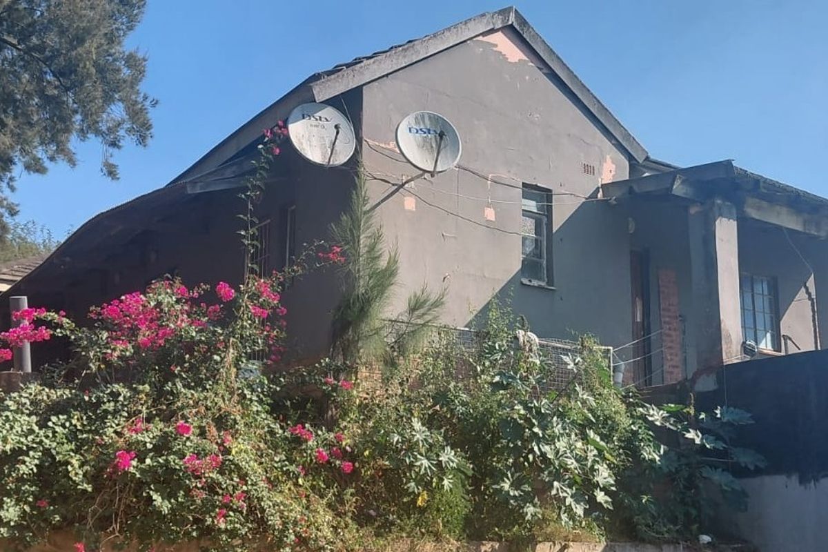 Rear exterior view of the house showing a weathered facade with peeling paint, satellite dishes, and a covered patio area.