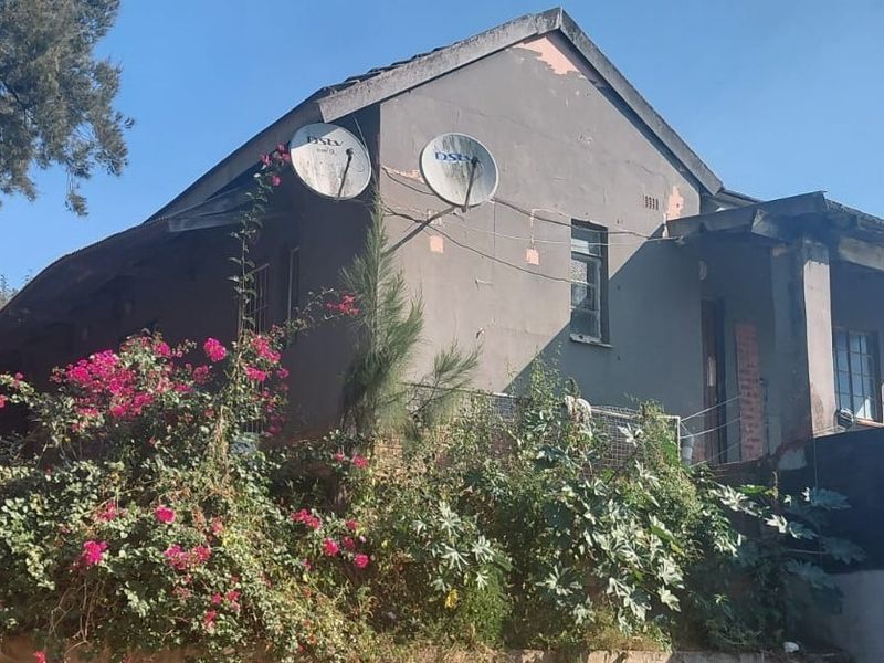 Rear exterior view of the house showing a weathered facade with peeling paint, satellite dishes, and a covered patio area.