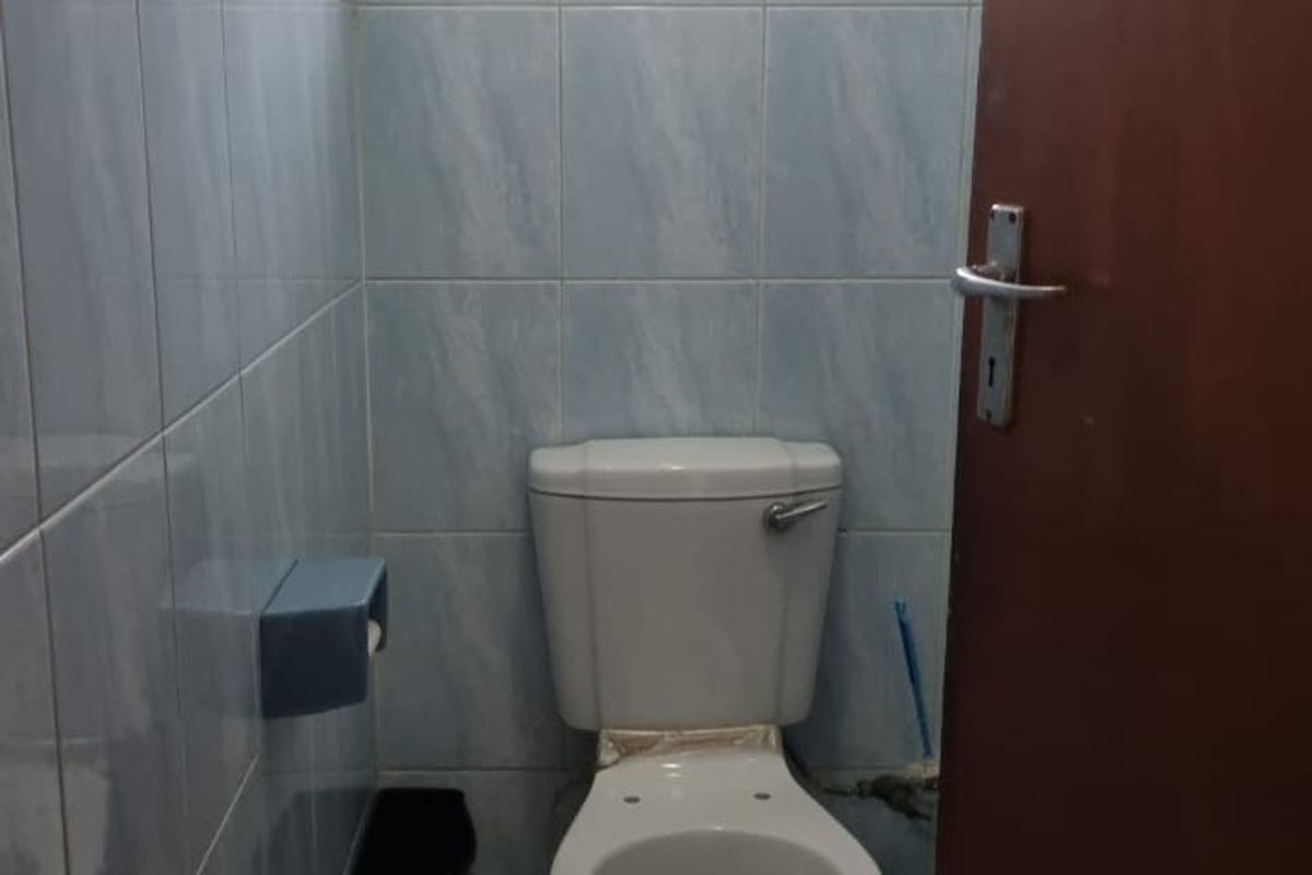 A compact, dated bathroom featuring light blue wall tiles, white floor tiles, and a standard toilet suite.