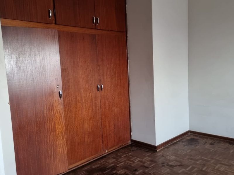 An empty bedroom featuring original parquet flooring and floor-to-ceiling built-in wooden cupboards, offering a blank canvas for renovation.