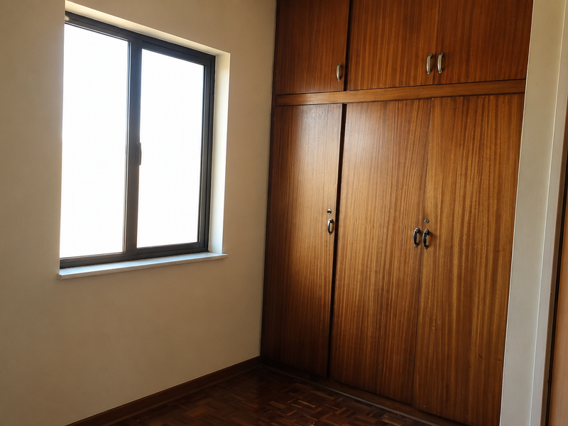 A bright, empty bedroom featuring classic parquet flooring and extensive built-in wooden cabinetry, offering ample storage space and natural light.