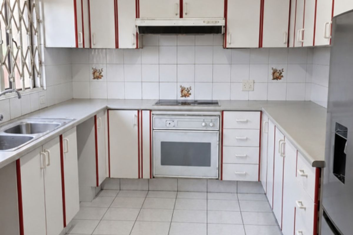 A functional kitchen featuring white cabinetry with red accents, tiled flooring, built-in oven, hob, and extractor fan, offering a clean and practical workspace.