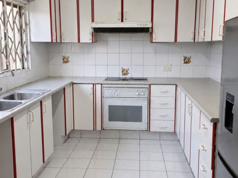 A functional kitchen featuring white cabinetry with red accents, tiled flooring, built-in oven, hob, and extractor fan, offering a clean and practical workspace.
