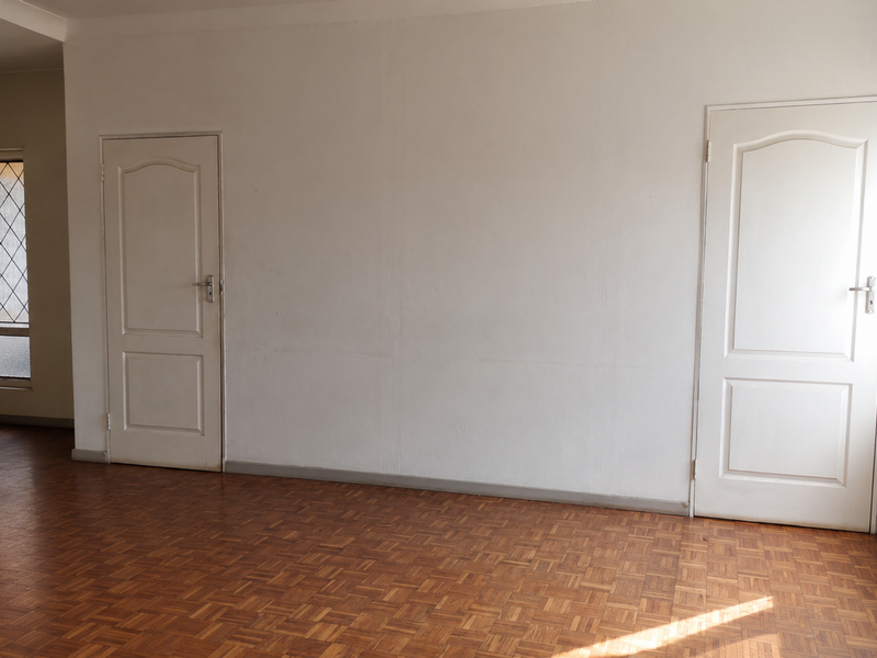 An empty living area featuring classic parquet flooring, neutral walls, and two internal doors, offering a blank canvas for interior design.